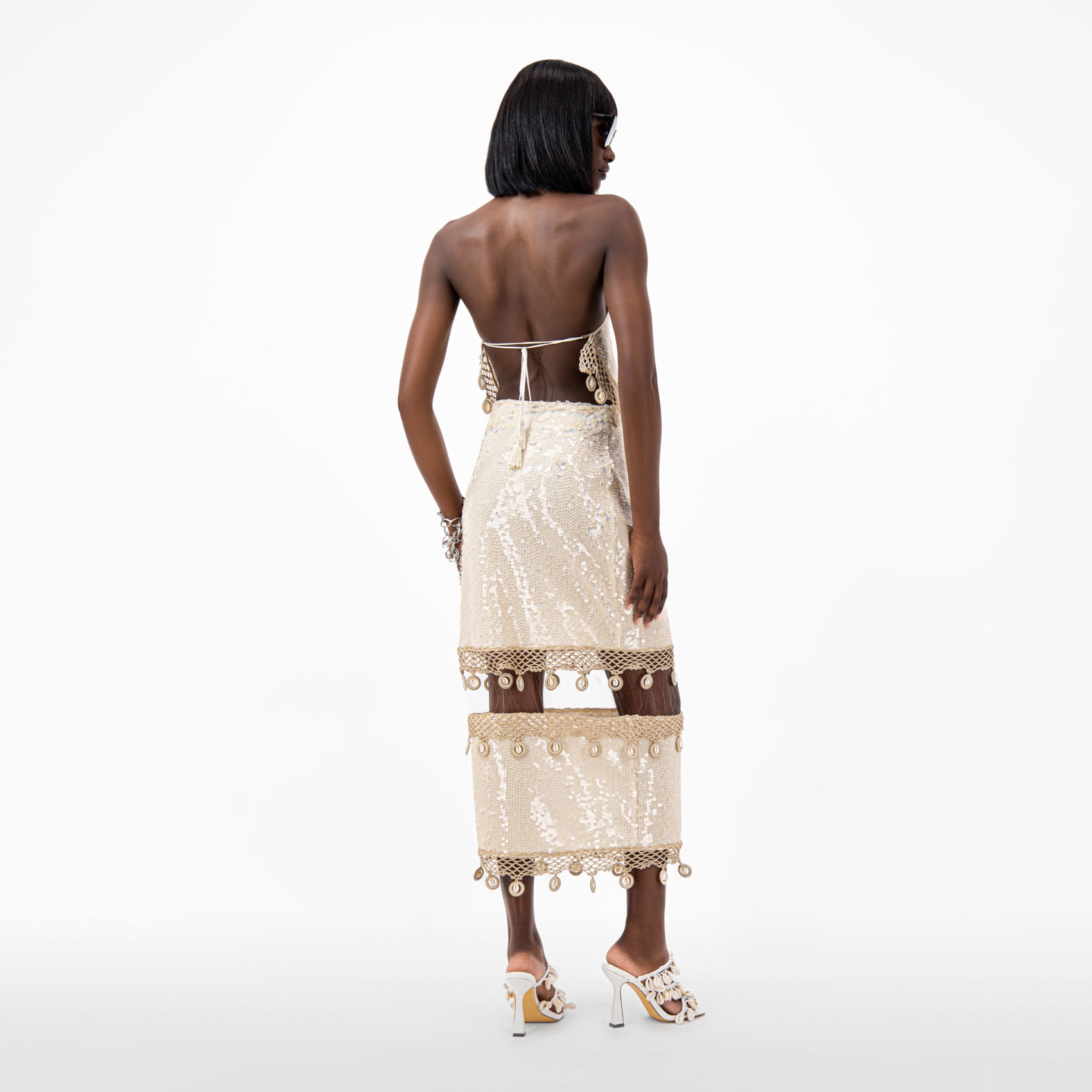 Back view of a model wearing the Sequin Halter Neck Crop Top with crochet hem and cowrie shell details.