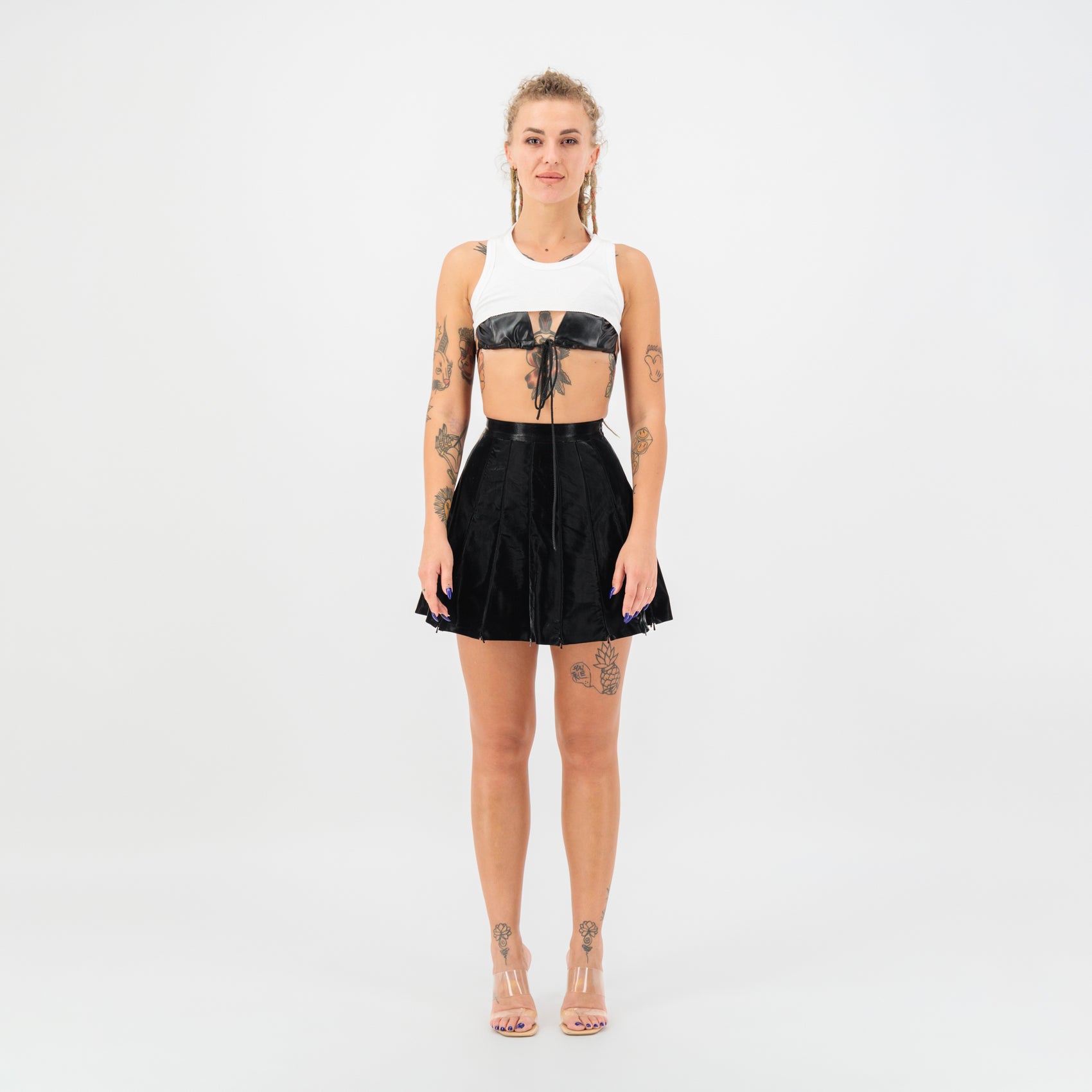 high waisted faux leather mini skirt worn by model with tattoos and casual outfit on a plain background.